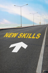 New skills written on black asphalt road with white arrow and marking lines for given direction on beach background. New skills development concept and changing skill demand idea