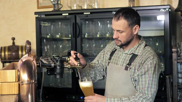 The bartender pours a light beer into a foaming glass. A row of beer steel taps in a dark pub or bar. Taps for draught beer in a modern bar. The bartender pours craft beer at the bar.