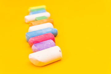 Children's drawing crayons lie in a row on a yellow background. Multi-colored chalk close-up.
