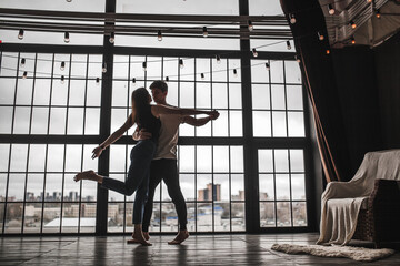 Fototapeta na wymiar a girl and a guy dance against the background of a huge window, the silhouette of a dancing couple