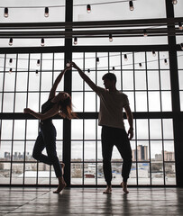 Fototapeta na wymiar a girl and a guy dance against the background of a huge window, the silhouette of a dancing couple