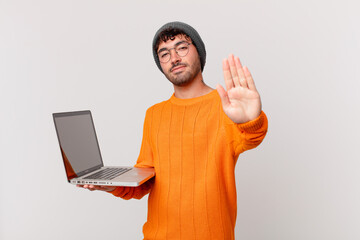 nerd man with computer looking serious, stern, displeased and angry showing open palm making stop...