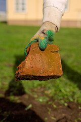 Focus on male hand presenting concrete block. Happy smiling constructor man in protective outfit holding red brick in one hand and looking at camera with gladness. Building concept