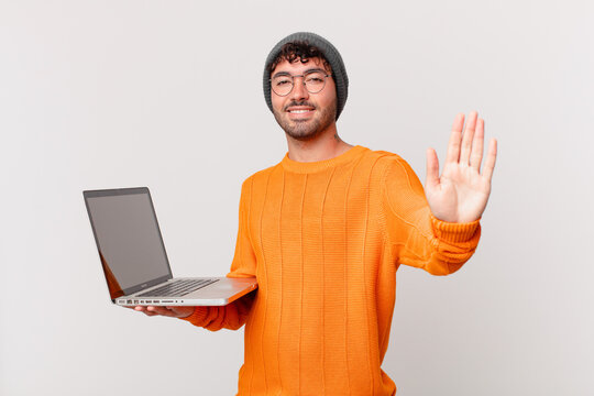 nerd man with computer smiling happily and cheerfully, waving hand, welcoming and greeting you, or saying goodbye