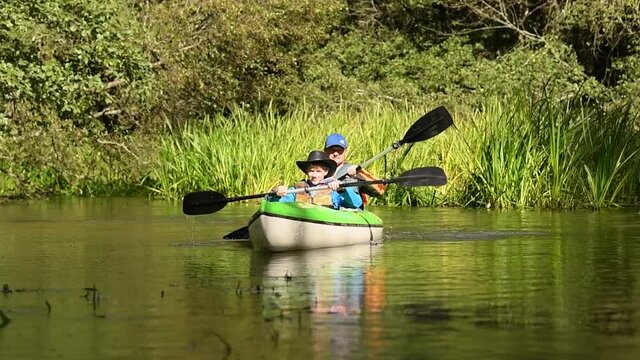Father and son paddling kayak at summer river