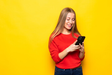 Beautiful young woman chatting by mobile phone isolated over yellow wall background.