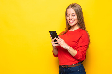 Young woman chatting by mobile phone isolated over yellow wall background.