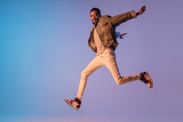 Young stylish man in modern street style outfit isolated on gradient background in neon light....
