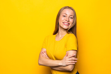 Obraz premium Portrait of a smiling blonde young woman standing with arms folded isolated over yellow background