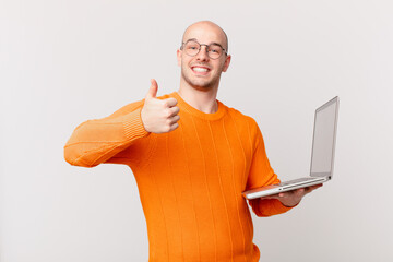 bald man with computer feeling proud, carefree, confident and happy, smiling positively with thumbs up