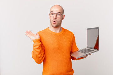 bald man with computer looking surprised and shocked, with jaw dropped holding an object with an...