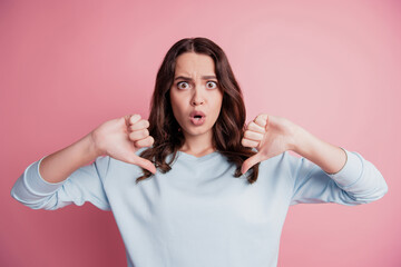 Young shocked stunned brunette girl showing two thumbs down open mouth on pink wall © Tetiana