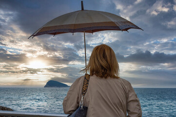 Woman with an umbrella looking at the horizon on the island of Benidorm, Spain