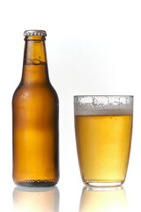 Brown beer bottle and a glass of beer in a white background. Beer brown bottle with drops and a full glass of beer isolated in white background