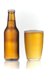 Brown beer bottle and a glass of beer in a white background. Beer brown bottle with drops and a full glass of beer isolated in white background