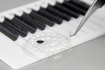 A tablet with false eyelashes, glue and tweezers on a gray background. Cosmetic accessories for...