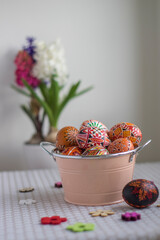 Homemade handmade painted Easter eggs in decorative old pink color tin on flowered tablecloth with flowering hyacinth flowers