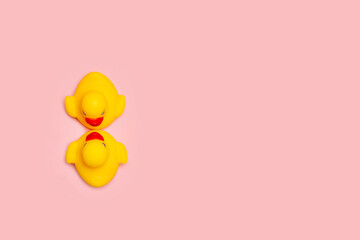 Dos patos de goma amarillos enfrentados dandose un beso sobre un fondo rosa pastel liso y aislado....