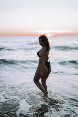 Chica guapa morena española en el sur de españa en una cala natural con piedras y olas salvajes disfrutando de un atardecer calido de verano 