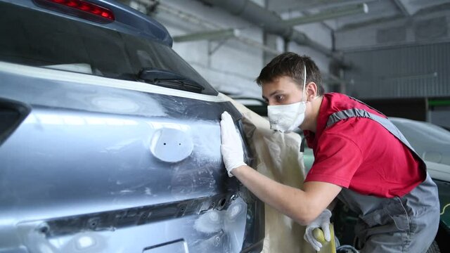 auto repairman makes surface preparation of automobile body
