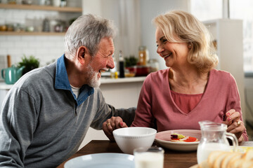 Senior couple eating breakfast in the kitchen. Husband and wife talking and laughing while eating a sandwich