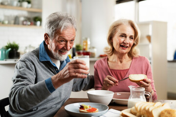 Senior couple eating breakfast in the kitchen. Husband and wife talking and laughing while eating a sandwich