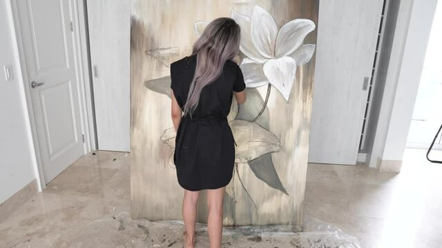 Beautiful female artist standing and working on painting in back static view