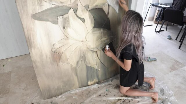 Latina female kneeling on ground and painting beautiful painting on canvas