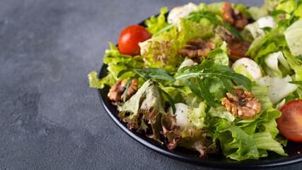 Diet salad with tomatoes, mozzarella cheese, arugula and walnuts on a plate. Copy space