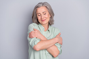 Photo of happy smiling beautiful dreamy lovely mature woman hug embrace herself isolated on grey...