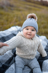 Mom holds the baby and plays with him on the street. Six month old baby in a hat, jacket and pants.