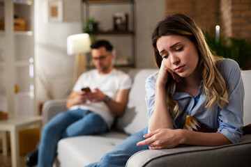 Fototapeta premium Couple at home after having a fight. Sad depressed woman sitting on sofa..