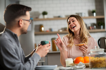 Happy girl enjoying in breakfast with her boyfriend. Loving young couple drinking coffee and eating sandwich at home.