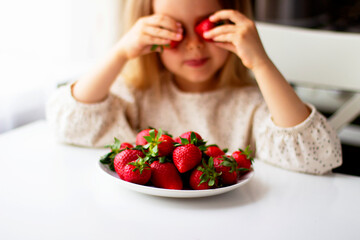 Obraz na płótnie Canvas Cute little girl eating fresh strawberry in the kitchen. Healthy vitamin snack for kids. Ripe fresh berries. Harvest season. Natural vitamins .