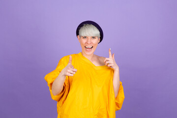 Stylish european woman on purple background point to you to camera with happy face