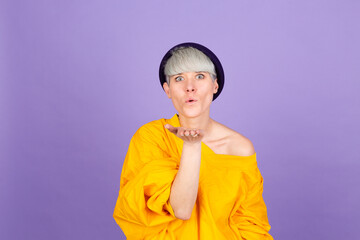 Stylish european woman on purple background smiling looking at the camera blowing a kiss with hand on air being lovely