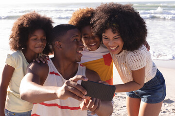 African american parents and two children taking a selfie with smartphone at the beach smiling