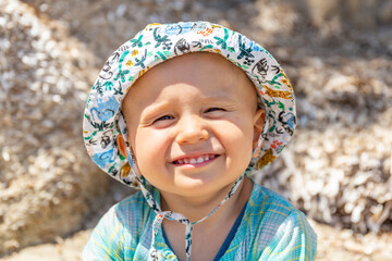 Close up portrait of a little boy in panama hat, outdoors in summer. Child squinting in the sun and smiling with pleasure.