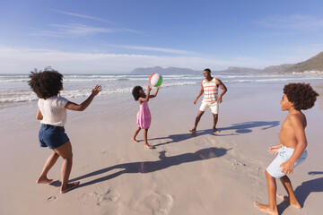 African american parents and two children having fun playing with ball at the beach