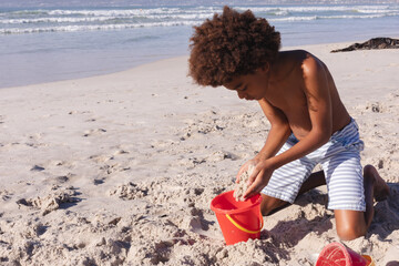 African american boy having fun playing with sand at the beach