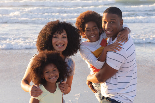 Portrait of smiling african american parents and two children embracing at the beach