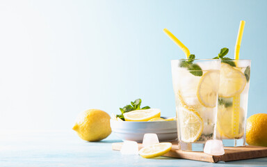 Two glass with lemonade or mojito cocktail with lemon and mint, cold refreshing drink or beverage with ice on blue background. Copy space