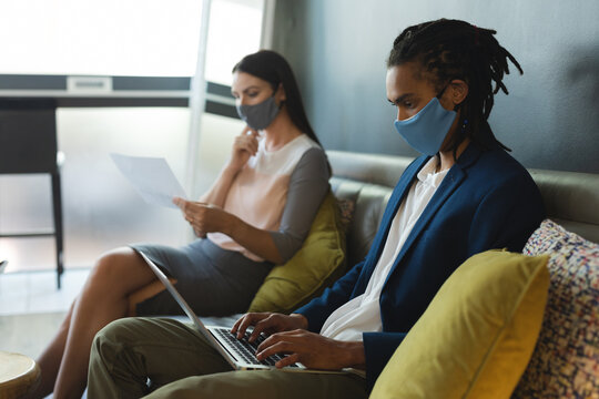 Diverse male and female of business colleagues wearing face masks sitting on sofa working