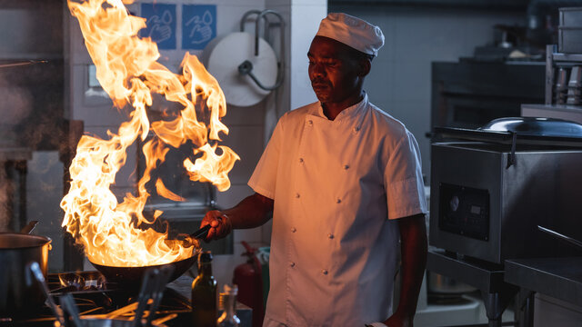 African american male professional chef flambeing dish in wok