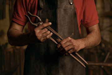 Blacksmith with metal tongs in smithy portrait
