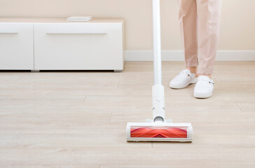 Housemaid hoovering laminate floor with modern vacuum cleaner in room