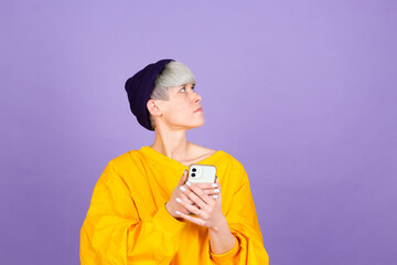 Stylish european woman on purple background with mobile phone thinking dreaming look up right