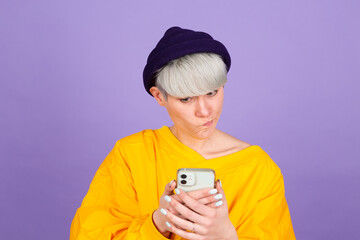 Stylish european woman on purple background feeling sad unhappy angry while reading sms using her mobile phone