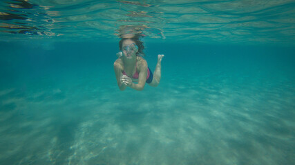A Girl Swimming Underwater Through The Turquoise Sea. Young Woman Enjoying Summer Activities.