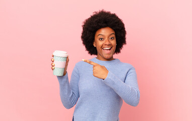 afro woman looking excited and surprised pointing to the side and upwards to copy space. coffee...